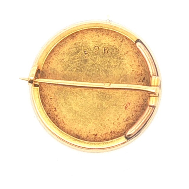 This brooch is crafted in 18k gold. The piece features a circular design with a detailed hand-painted enamel portrait of...