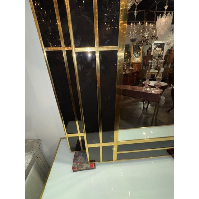 This modern Italian designer mirror features a sleek black glass frame with polished brass accents, adding a touch of...