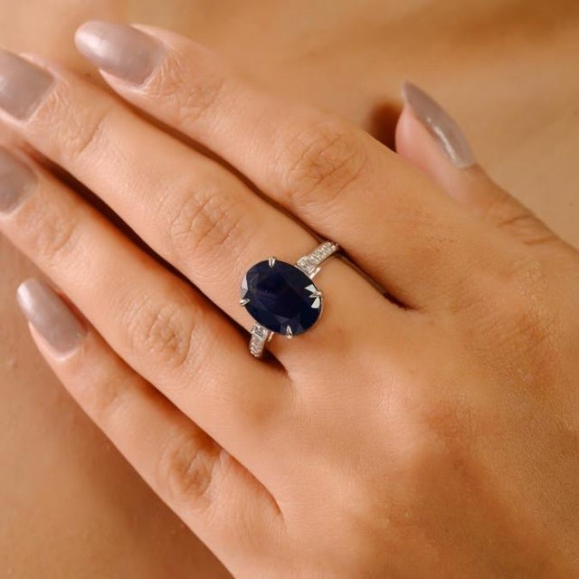 This elegant engagement ring features a stunning 5-carat oval-cut deep blue sapphire as the centerpiece, securely held by...