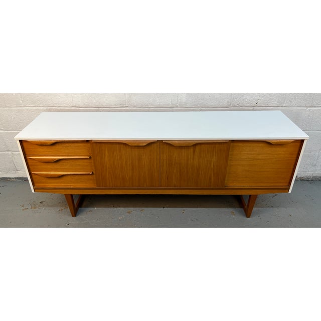 This vintage Mid-Century Modern sideboard was manufactured by Stonehill Furniture in England and features distinctive sled...