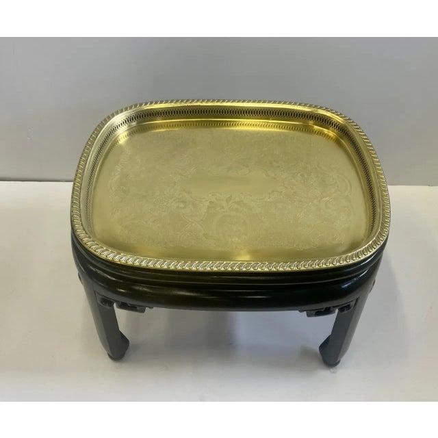 Handsome brass tray top cocktail table having ebonized base with carved apron having Asian flair.