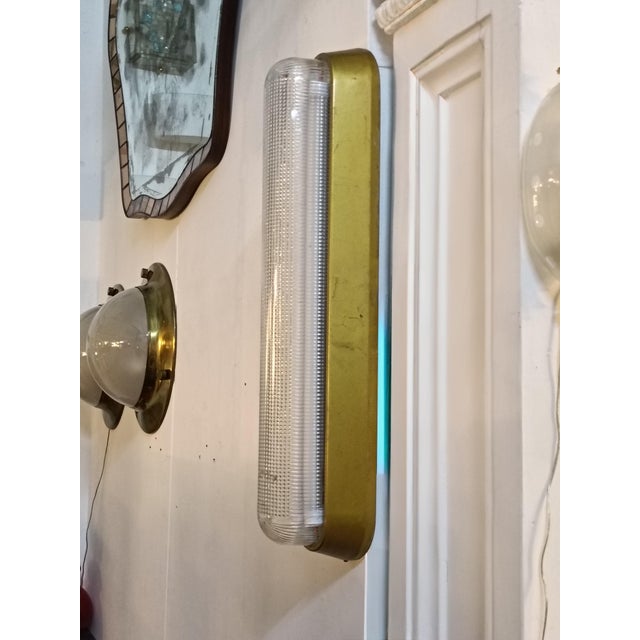 Wall lamp with a gold metal frame and a ribbed or textured glass tube shade. This style is often associated with Art Deco...