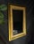 Ornate giltwood-style wall mirror with an Egyptian Revival inspired design. The rectangular frame features a wide gold-...