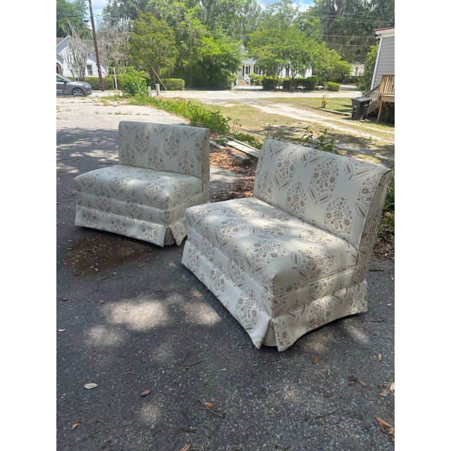 A charming pair of upholstered banquette lounge chairs featuring a tailored skirted base and soft, armless silhouette....