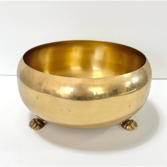 A classic vintage brass planter bowl resting on sculpted claw feet, offering timeless Hollywood Regency style. The warm...