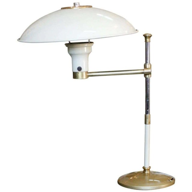 High style Mid-Century desk lamp with an enameled Frostine white steel body and brass accents. The lamp features an...