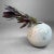 A restrained, spherical ikebana vase with a soft, almost cloud-like presence. The fine craquelure glaze shifts subtly from...
