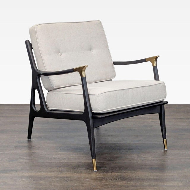 This stylish lounge chair from Anthropologie features a sleek black wood frame with brass accents on the arms and legs....
