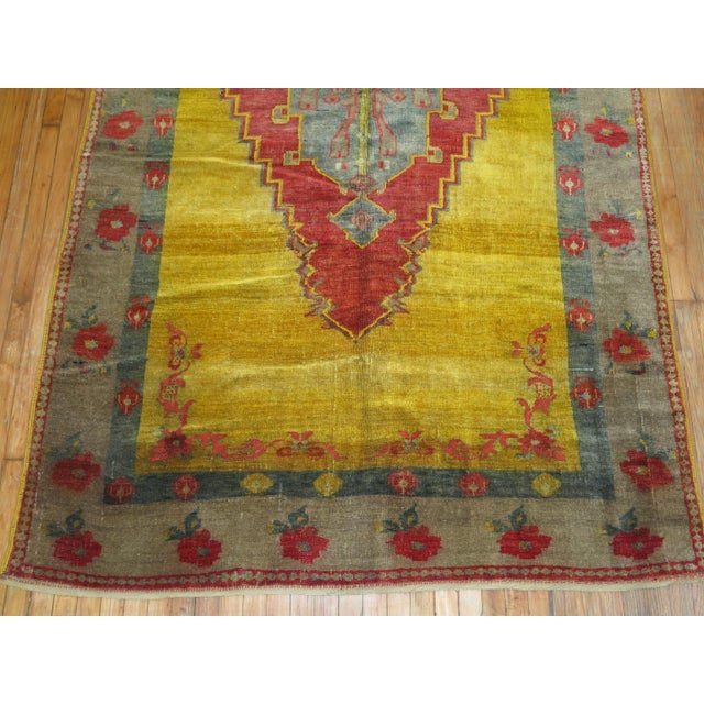 A highly unusual Turkish rug with a large red medallion in soft red on a sunny yellow field with a pretty grayish floral...
