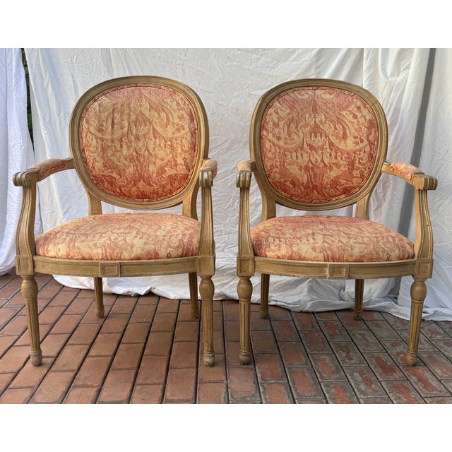 This striking pair of Louis XVI style arm chairs feature molded medallion backs and fluted circular legs. The wood frame...