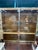 Two available- This Hollywood Regency display cabinet features smoked glass doors and shelves framed in polished brass...