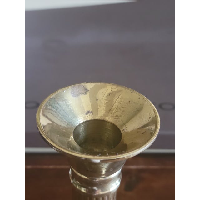 Neoclassical Corinthian polished brass column candlestick holder featuring a fluted stem and a square, tiered base.