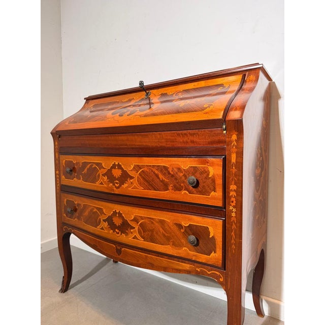 Elegant secretary desk in warm walnut veneer, richly decorated with refined marquetry inlays. The drop-front writing...