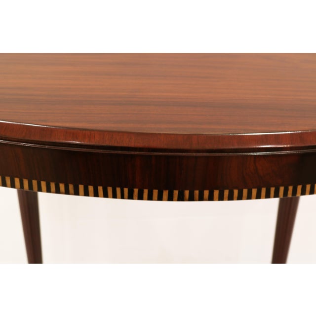 An Art Deco oval lamp table with tapered fluted legs, fruitwood and ebony inlay details surround the apron.