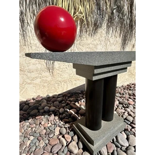 The Memphis Style Tubular Black Pedestal with Gray Stucco Finish Top with a Red Sphere Console Table is a sleek and retro...