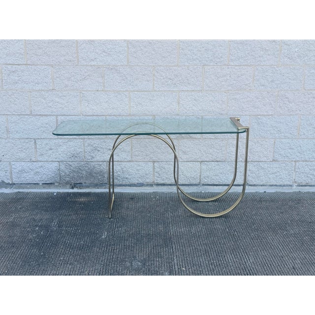 Postmodern console table with a sculptural curved flat-bar base in a brass-finish metal. The base is formed from...