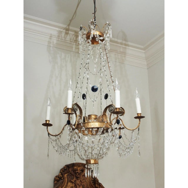 A gilt tole, six light chandelier, likely Tuscan, suspended from beaded ropes attached to scrolling acanthus supports, the...