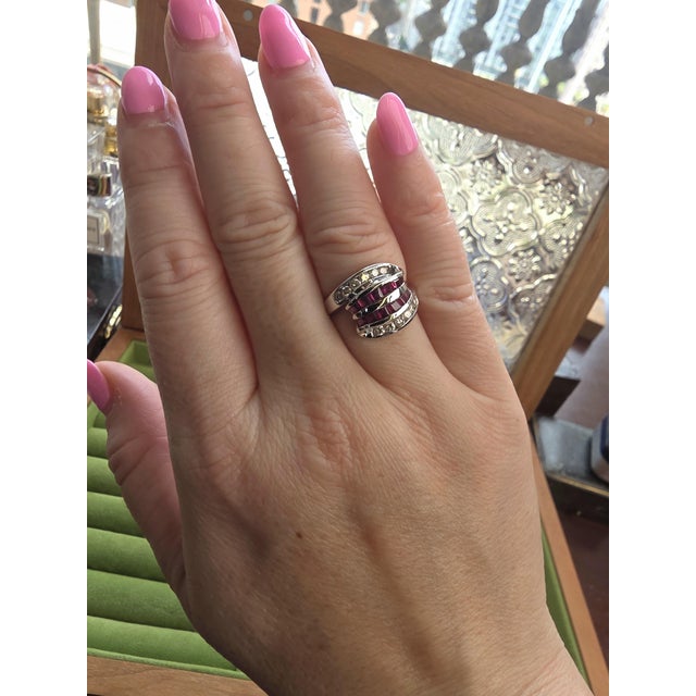 This estate ring features a clean, structured design with alternating channel-set rubies and diamonds. The vivid red...