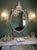 All white mother-of-pearl inlaid wall mirror featuring an elegant oval silhouette and ornate crown crest. The frame is...