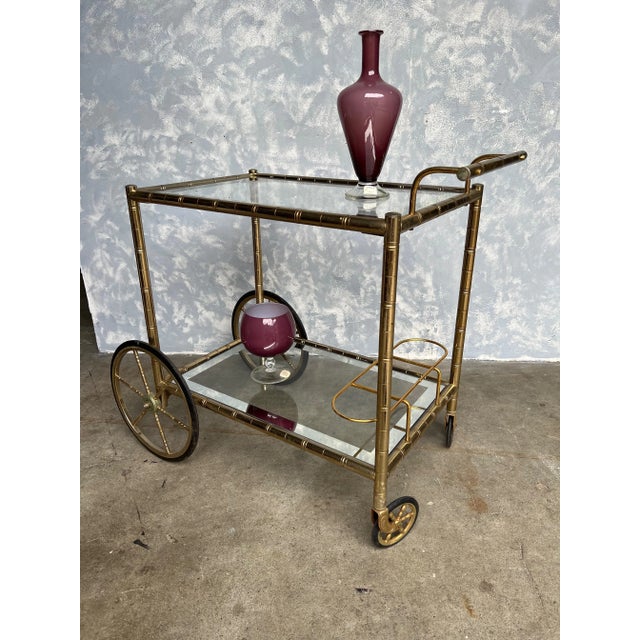 An elegant French brass and glass bar cart from the 1950s. The brass frame has a stylized bamboo motif and is supported on...