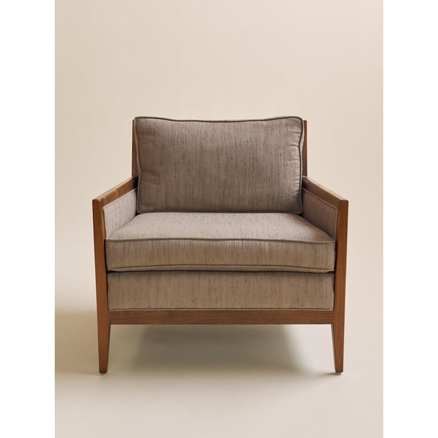A clean-lined mid century lounge chair with a walnut frame and tailored beige upholstery. The broad seat, angled arms, and...