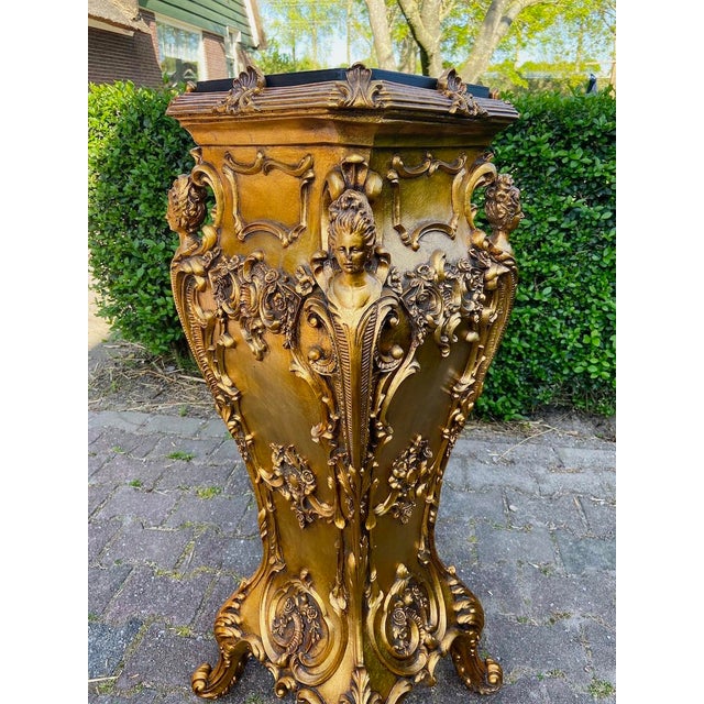 A dramatic 1990s Italian Baroque-style pedestal, richly decorated in a gold finish with a dark marble-effect top. This...
