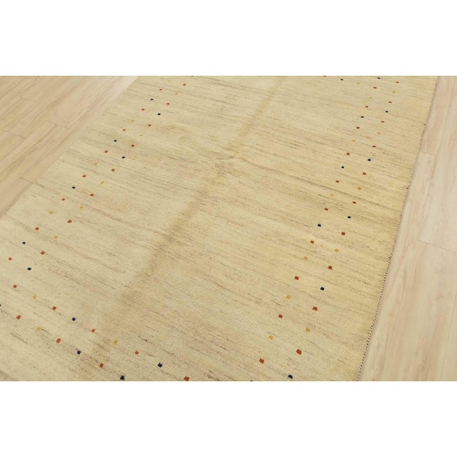 A contemporary Gabbeh rug hand-knotted with an all-wool pile on a cotton foundation. This area rug features a solid beige...