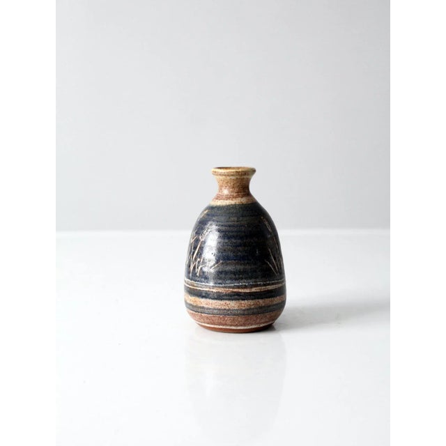 A vintage studio pottery vase, hand-crafted with a graceful bottleneck silhouette. The surface features a layered blue and...