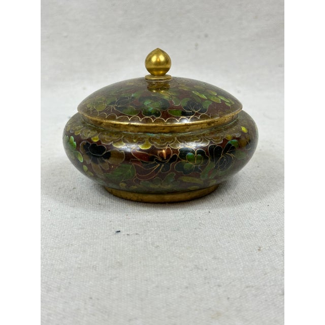 Vintage cloisonne box with lid beautifully decorated with flowers and leaves in shades of green on an oxblood background...