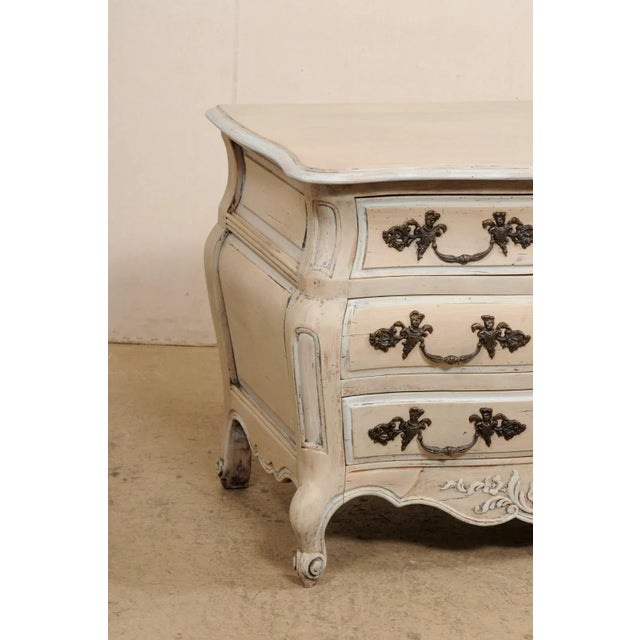 A French carved and painted-wood chest of three drawers. This vintage chest from France features a curvy bombé style case,...