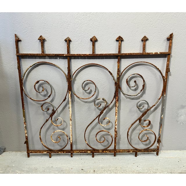 This vintage ornate wrought iron gate features decorative scrollwork and pointed finials. Significant rust and gray paint...