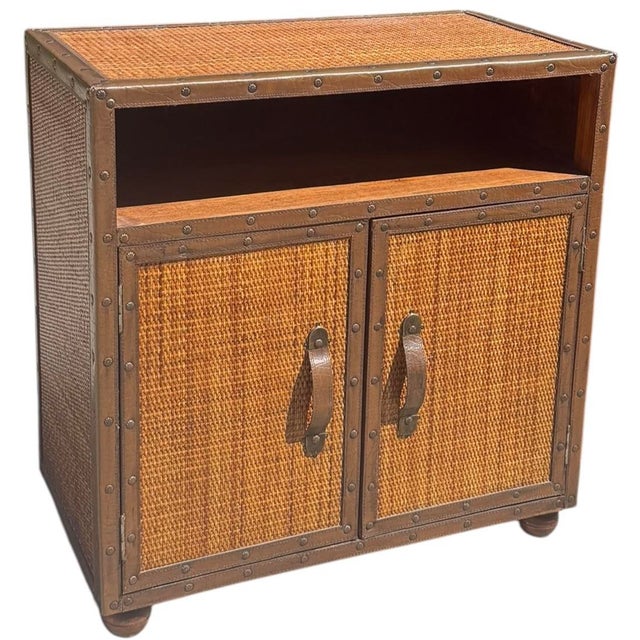 Vintage campaign-style console cabinet featuring woven rattan panels across the top, sides, and cabinet doors. The warm...