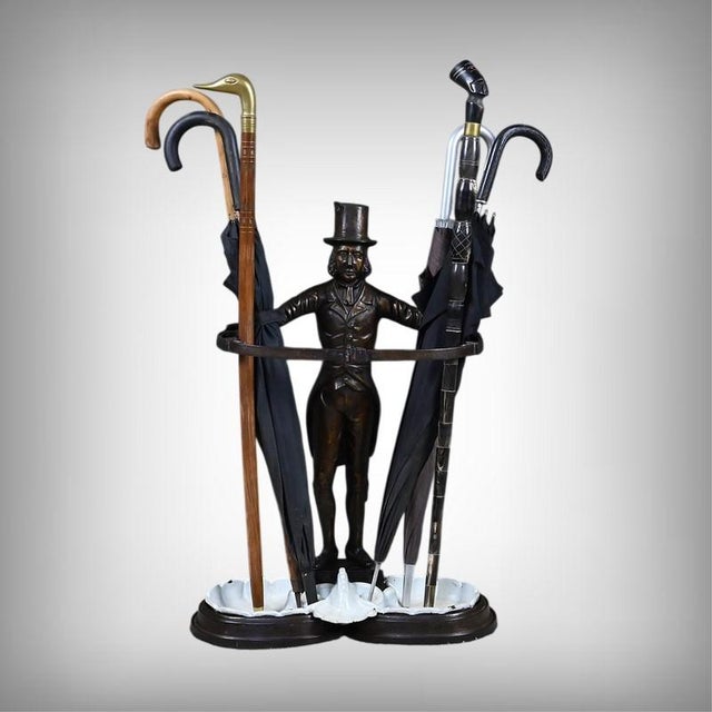 This cast iron umbrella stand or walking stick holder depicts an elegantly dressed gentleman, wearing a top hat and a...