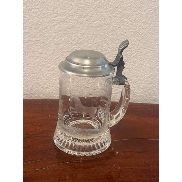 This elegant vintage German beer stein features a clear glass body with an etched Equestrian Horse motif, topped with a...