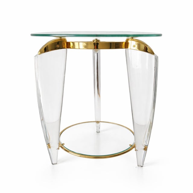 Elegant side table featuring a circular glass top, clear acrylic legs, and polished brass details. The sophisticated...