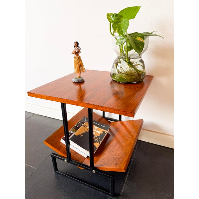 This mid-century modern magazine table in wood and black metal features a graphic, architectural design with a square top...