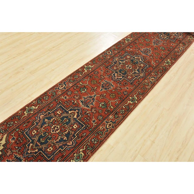A traditional tribal Heriz runner hand-knotted with an all-wool pile on a cotton foundation. This oriental rug features a...
