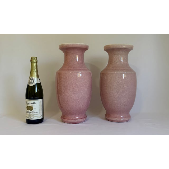 A striking matched pair of tall ceramic vases finished in a soft blush-pink crackle glaze. The dense network of fine...