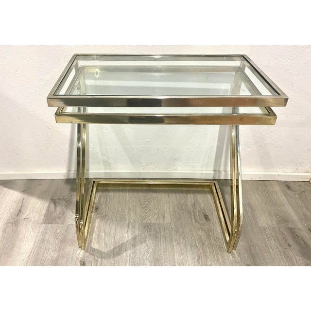 Pair of brass cantilever framed nesting side tables with glass tops, in the style of Milo Baughman. Square tube brass...