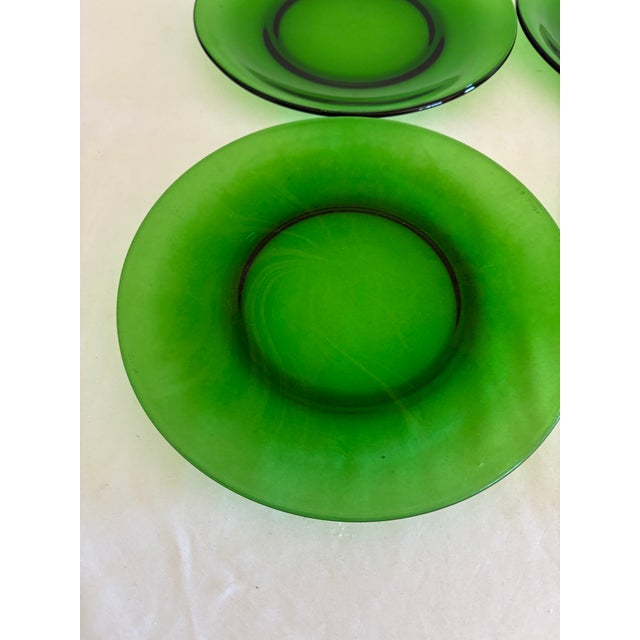 A set of four vintage emerald green glass plates from Vereco, France. Each has a wide, softly sloped rim and a smooth...