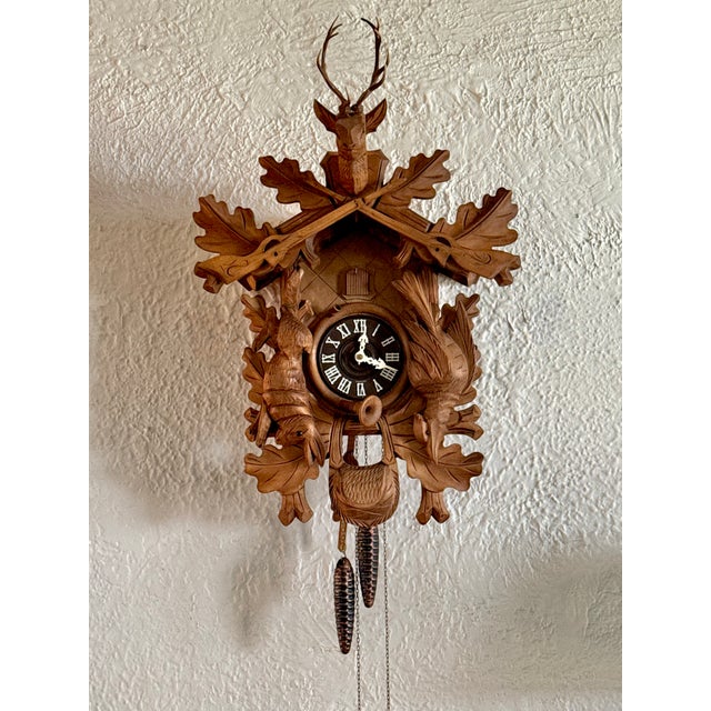Black Forest style German cuckoo clock with hunter's trophy motif of stag, rifles, rabbit, and pheasant. Animals have...