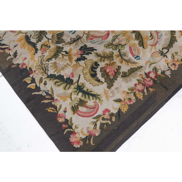 This charming antique English needlepoint rug, dating back to the 1920s, captures the whimsical vitality of nature in a...