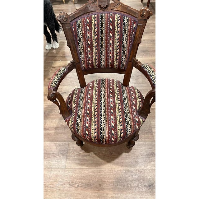 This antique armchair features intricately hand-carved wood accents, turned front legs, padded armrests, and vibrant...