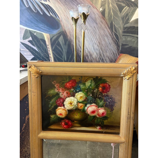 Classic 1985 Trudeau mirror featuring a floral still life painting above a beveled mirror, framed in carved gilt wood with...
