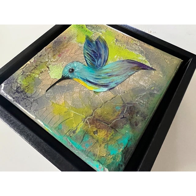 This artwork features a vibrantly colored hummingbird, gracefully poised against a textured background of soft greens and...