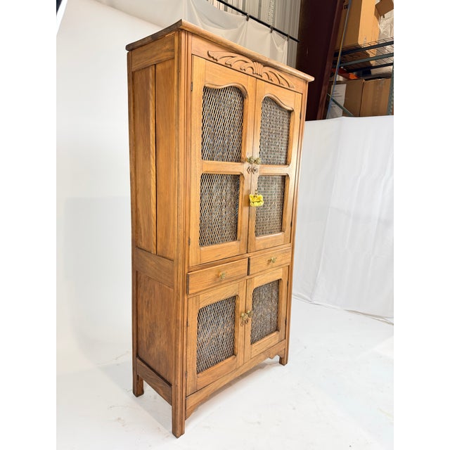 This is a handsome vintage wood cabinet distinguished by woven cane panel doors and elegant carved detailing along the...