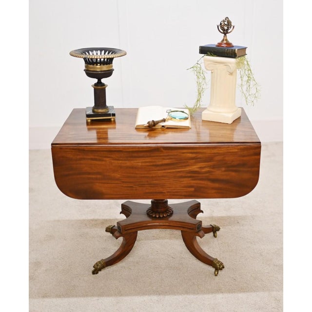 A Regency drop leaf Sutherland table in mahogany supported by a platform base Features splay legs terminating in brass...
