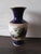 An ornate ceramic vase featuring a bucolic landscape scene with figures. The main body of the vase is a dark, rich blue,...