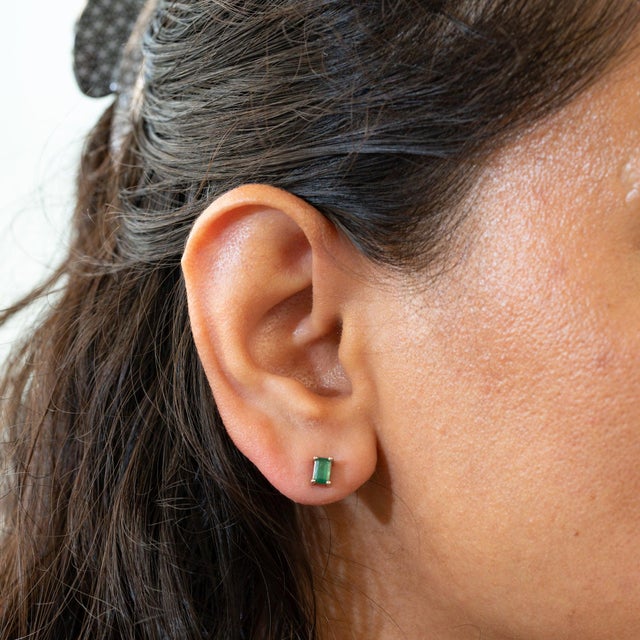 A matched pair of Zambian emeralds shines in rich, saturated green in these emerald-cut solitaire stud earrings, crafted...
