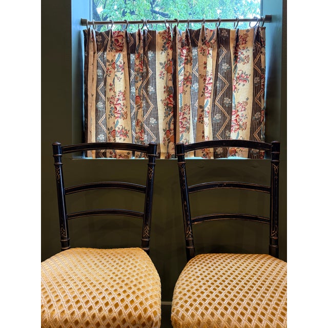 This pair of black wooden chairs features decorative gold painted detailing along the ladder backs and turned legs. The...